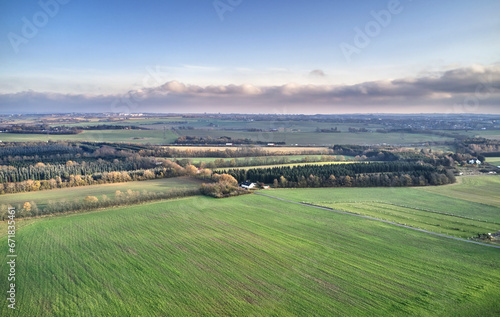 Serene landscape of endless grass fields with trees in the peaceful and quiet countryside against vibrant blue horizon with copy space. Aerial view of rural farm land on a cloudy summer day in Europe