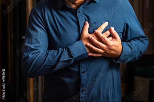 Heart attack. Man in blue shirt clutching his chest from acute pain. Heart attack symptom. Severe heartache, man suffering from chest pain, having heart attack or painful cramps, pressing on chest