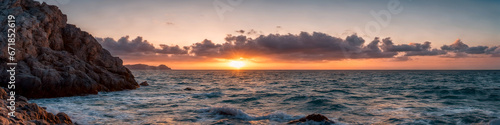 A sunset over the ocean with small waves crashing on the shore and rocks in the water. Seascape illustration with cloudy sky and setting sun. Generative AI