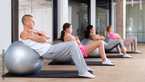 Focused young adult man doing workout with fitness ball during group pilates training photo