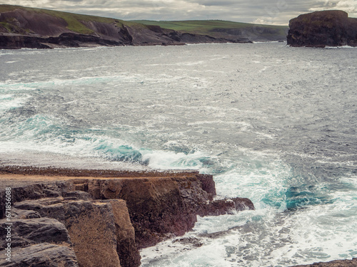 Powerful waves hit rough stone coast with cliffs and ocean scene. Ireland, Kilkee area. Travel, tourism and sightseeing concept. Irish landscape and nature scene. Nobody. Dramatic nature view. photo