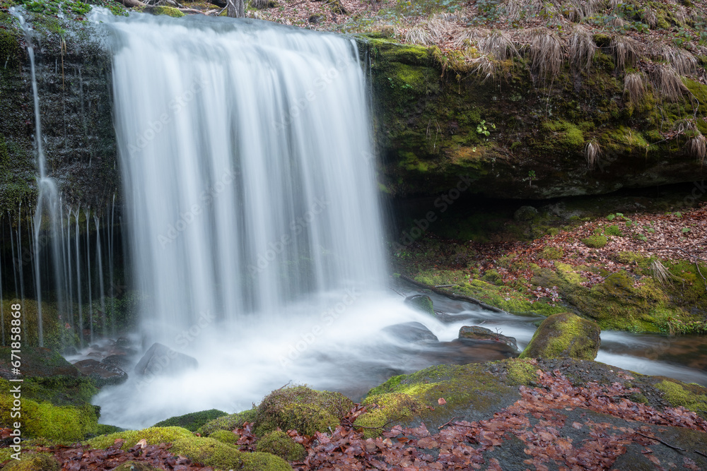 Obraz premium Beautiful long exposure blurred motion waterfall, dark, wet cliff and red Autumn colored leaves