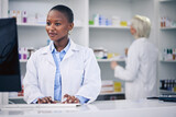 Pharmacist, typing and black woman on computer in pharmacy, drugstore or shop. Wellness, medical professional and African doctor on internet for telehealth email, healthcare and research for medicine
