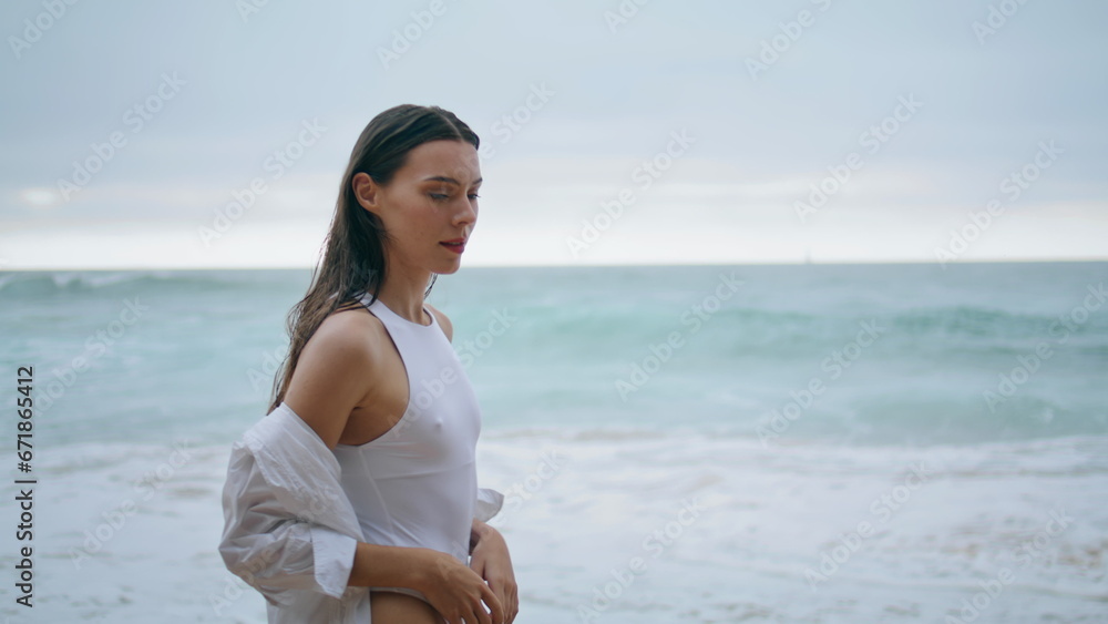 Lady walking cloudy shore in white swimsuit closeup. Woman posing in front ocean