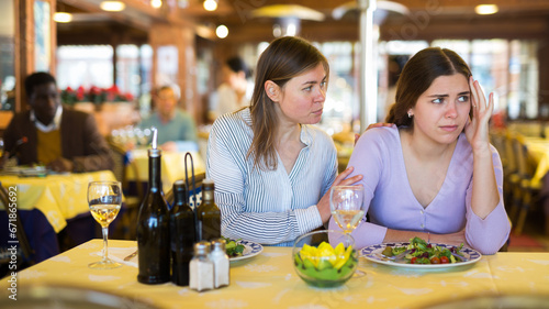 Woman comforting her upset female friend during friendly meeting over dinner in restaurant..