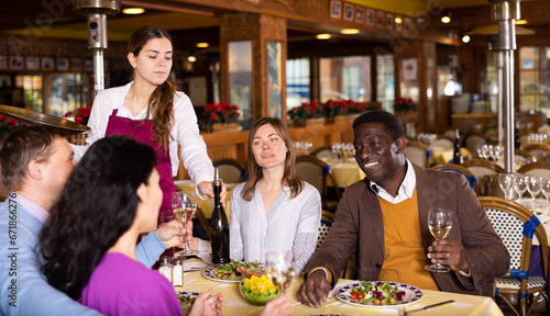 Group of joyous friends enjoying evening meal at cozy restaurant