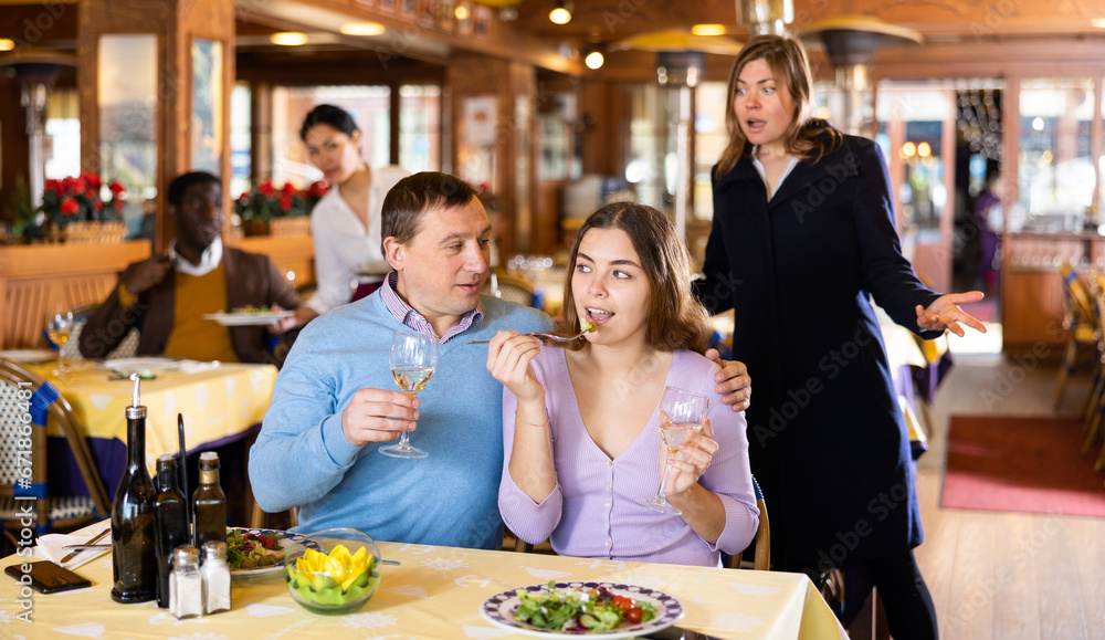 Resentful wife scolding her husband spending time with another woman at dinner in restaurant