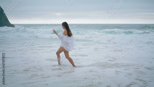 Playful girl running sea waves enjoying cloudy weekend. Woman jumping on beach.