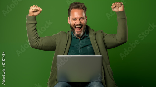 Portrait of a happy mature man using laptop computer while sitting on green background