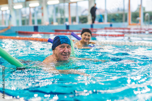 lovely European couple having swimming lesson with swim noodles in the indoor pool. High quality photo