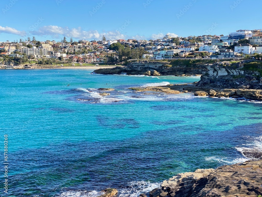 Bay and coastline next to the ocean. View of the city in the distance. View of turquoise waves breaking on the shore. Rocky coast of the ocean. Landscape and shore. Australia, Sydney.