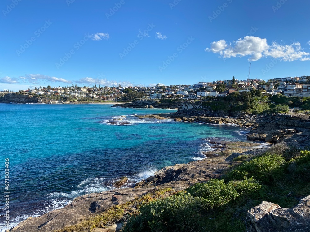 Bay and coastline next to the ocean. View of the city in the distance. View of turquoise waves breaking on the shore. Rocky coast of the ocean. Landscape and shore. Australia, Sydney.