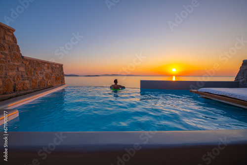 Tourist enjoys at the infinity swimming pool villa at sunset time, Mykonos, Greece © Kyrenian