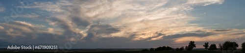 A landscape with an enchanting sunset. Panorama. Tragic gloomy sky. The last flashes of the sun on the storm clouds.