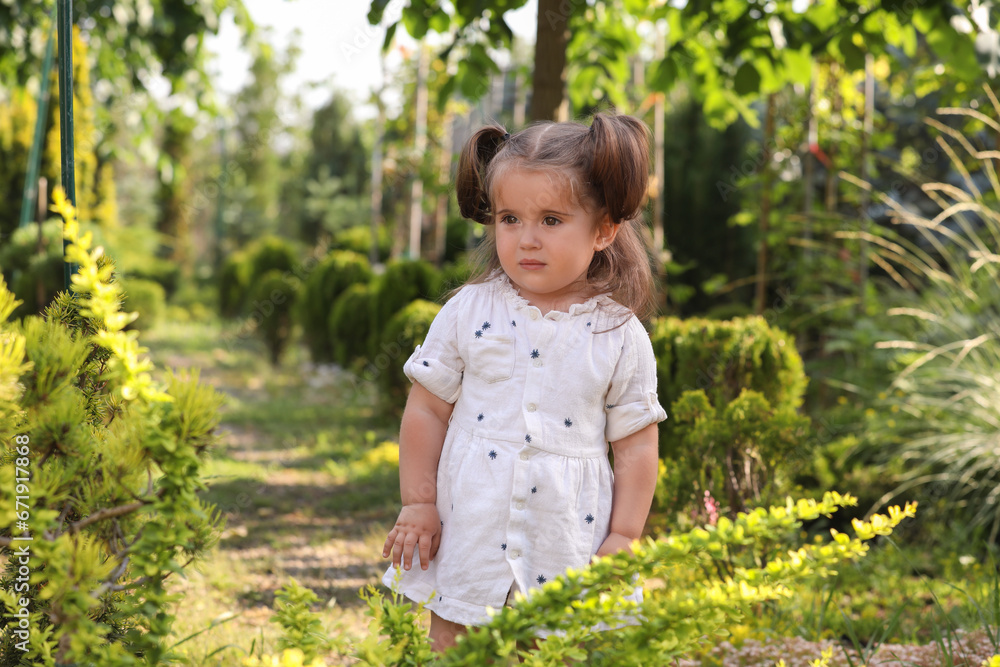 Cute little girl walking near green plants in park Cute little girl walking near green plants in park