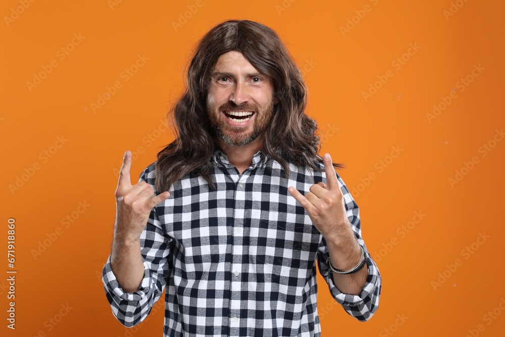 Hippie man showing rock gesture on orange background Hippie man showing rock gesture on orange background