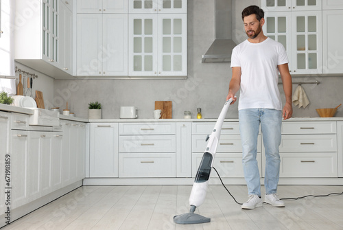 Happy man cleaning floor with steam mop in kitchen at home. Space for text