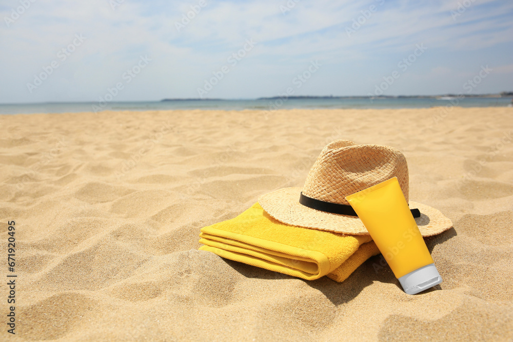 Sunscreen, towel and straw hat on sandy beach, space for text. Sun protection