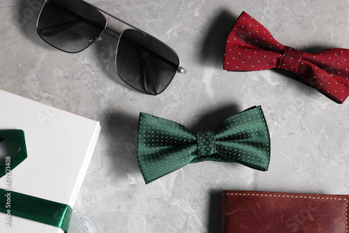 Stylish color bow ties, box, wallet and sunglasses on gray marble background, flat lay photo