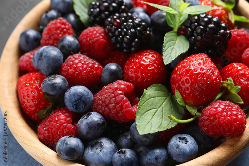 Many different fresh ripe berries in wooden bowl on black table, closeup