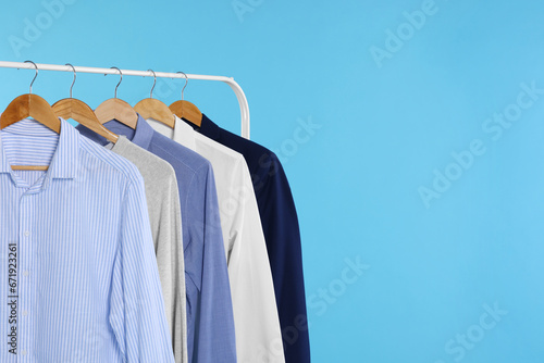 Rack with stylish clothes on wooden hangers against light blue background, space for text © New Africa