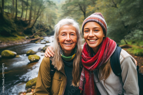 Young woman and her grandmother hiking together in the forest, with a calm stream flowing in the background. Adventures and bonding create a cherished moment in nature's embrace © MVProductions