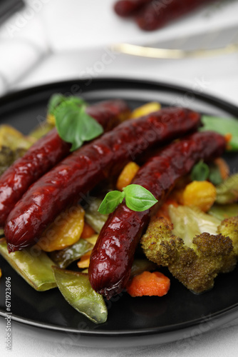 Delicious smoked sausages and baked vegetables on black plate, closeup