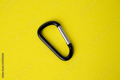 One black carabiner on yellow background, top view