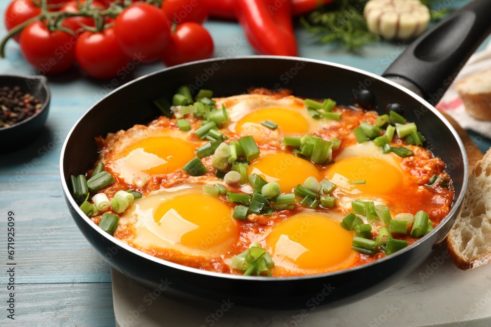 Delicious Shakshuka in frying pan on light blue wooden table, closeup
