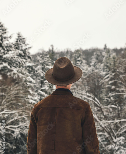 Man wearing a hat looking towards woods in the winter