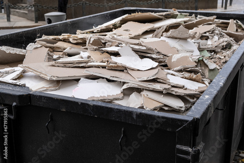 an overloaded dumpster waste container, with construction waste and drywall plasterboard, debris generated during the reconstruction process.