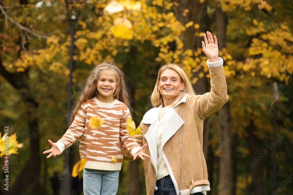 Fototapeta premium Happy mother and her daughter playing with dry leaves in autumn park