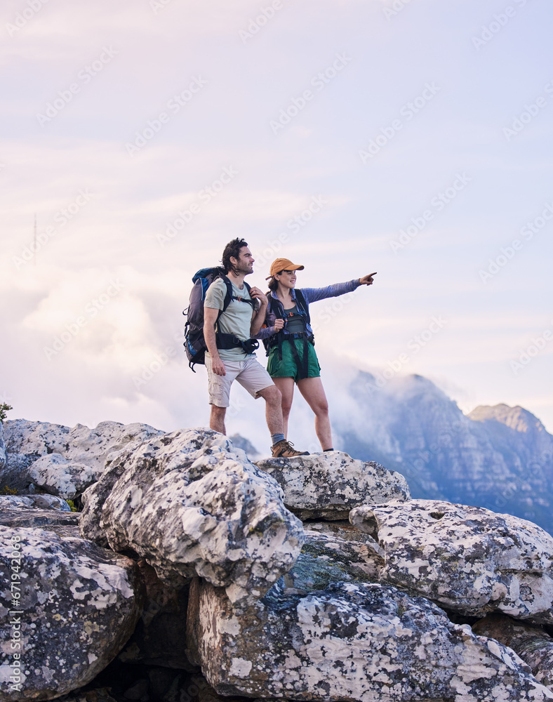 Mountains, hiking and pointing, man and woman on peak for adventure in nature, landscape and travel. Outdoor trekking, couple on cliff and relax in scenic clouds for natural journey, view and looking