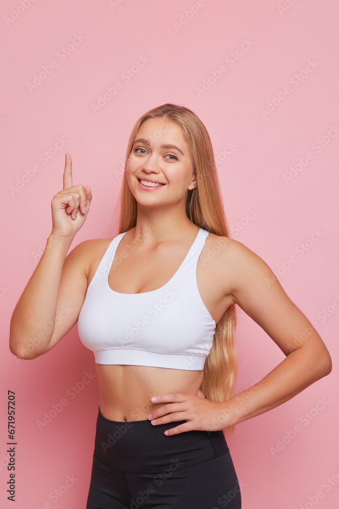 Beautiful sportsgirl with long blondehair posing in pink studio pointing finger up, Beauty and Health concept, copy space Beautiful sportsgirl with long blondehair posing in pink studio pointing finger up, Beauty and Health concept, copy space
