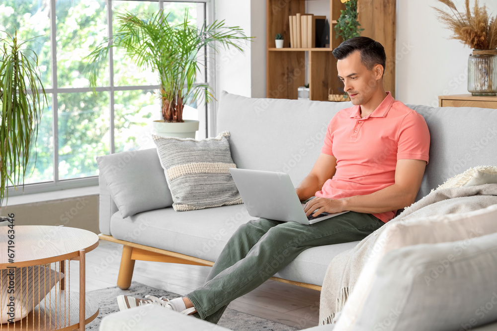 Handsome man using laptop while sitting on sofa in living room Handsome man using laptop while sitting on sofa in living room