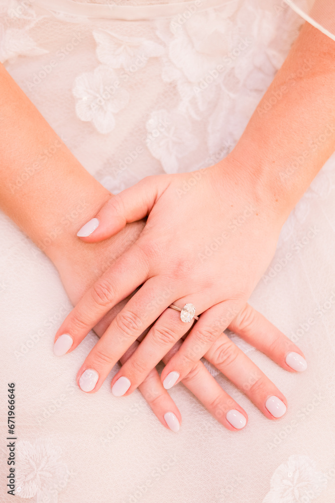 Fototapeta premium A bride has her hands folded over one another showing off her solitaire engagement ring