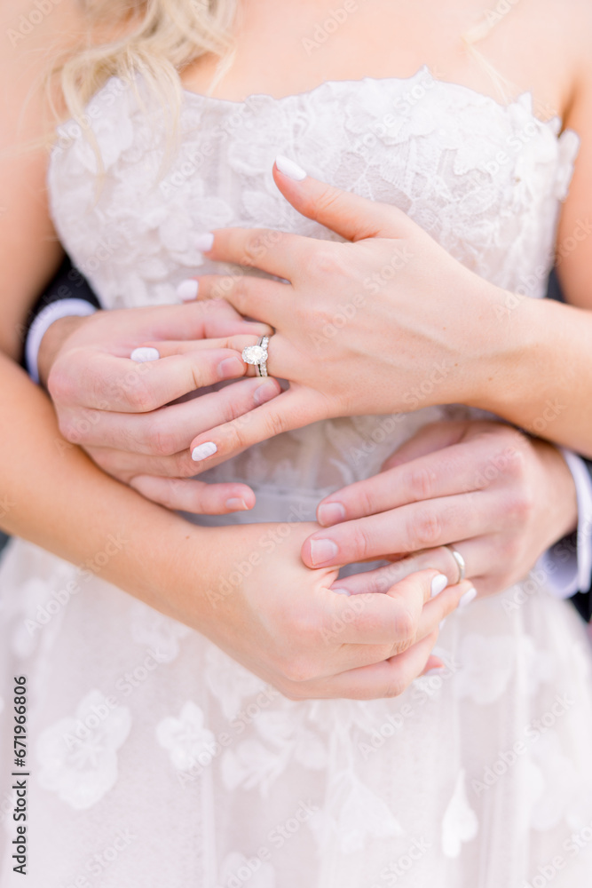 A bride and groom stand together touching their wedding bands A bride and groom stand together touching their wedding bands
