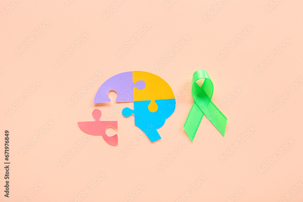 Colorful puzzle pieces in shape of brain with green awareness ribbon on pink background. Mental Health Day