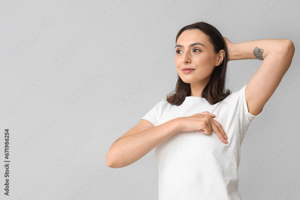 Young woman checking her breast on light background. Cancer awareness concept Young woman checking her breast on light background. Cancer awareness concept