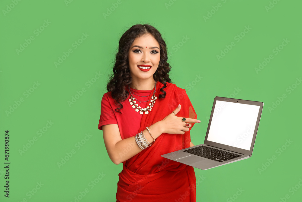 Naklejka premium Beautiful Indian woman in sari pointing at laptop on green background
