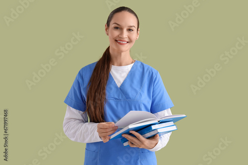 Female medical intern with books on green background