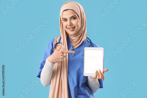 Muslim female doctor in hijab pointing at blank tablet screen, smiling health...