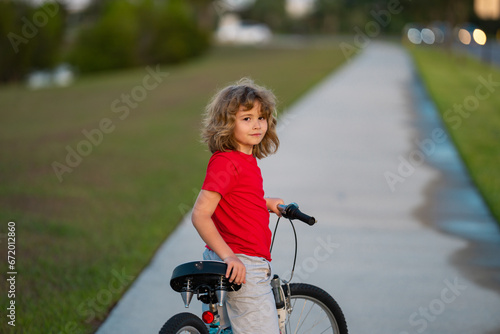 Kid boy riding a bike in summer park. Child drive a bike on a driveway outside. Kid riding bikes. Child on bike outdoor. Kid bicycling bike on american neighborhood.