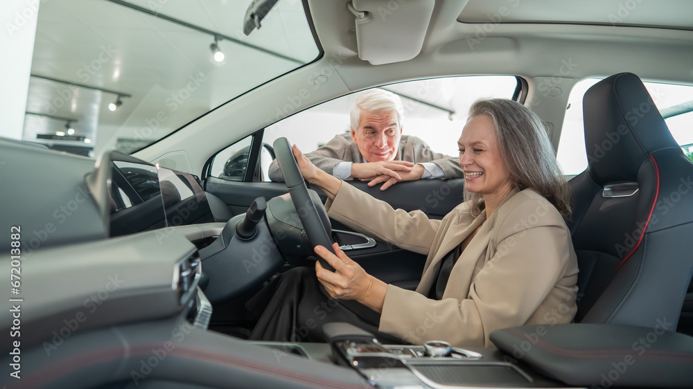 An elderly couple chooses a new car at a car dealership. Mature woman driving. An elderly couple chooses a new car at a car dealership. Mature woman driving.