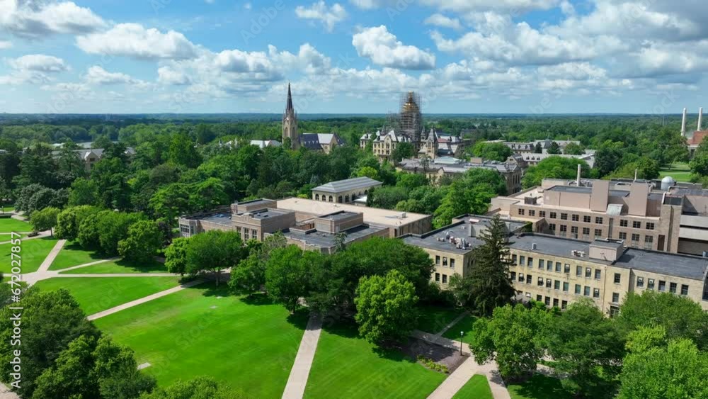 University of Notre Dame campus on beautiful summer day. Aerial descending shot above green lawn with Basilica of the Sacred Heart steeple and Main building golden dome. University of Notre Dame campus on beautiful summer day. Aerial descending shot above green lawn with Basilica of the Sacred Heart steeple and Main building golden dome.