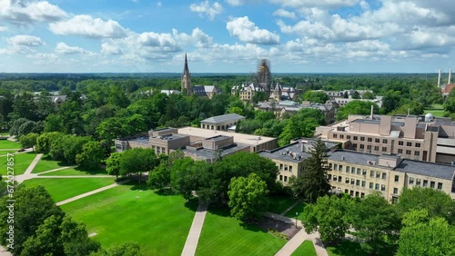 University of Notre Dame campus on beautiful summer day. Aerial descending shot above green lawn with Basilica of the Sacred Heart steeple and Main building golden dome. photo