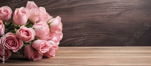 Close up photograph of a lovely arrangement of pink roses displayed in a vase on a rustic wooden table © 2rogan
