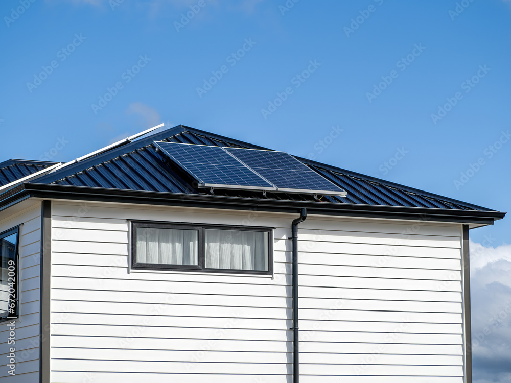 Solar panels on concrete tile roof of residential house with white wooden plank walls.