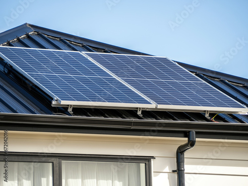 Solar panels on concrete tile roof of residential house with white wooden plank walls.
