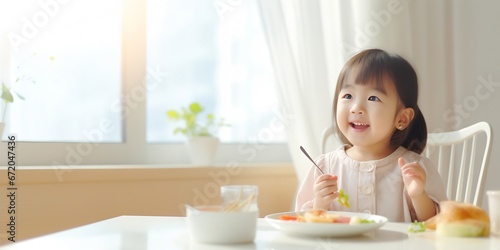Asian cute little girl holding fork and trying to eat food sitting on the white high chair in the morning at home with copy space.   Generative AI